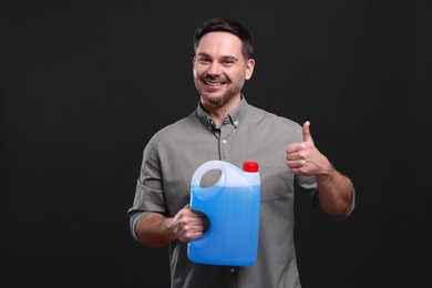 Man holding canister with blue liquid and showing thumbs up on black background