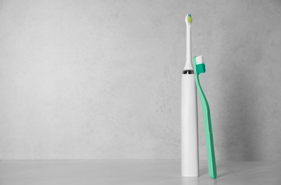 Photo of Electric and plastic toothbrushes on light background, space for text