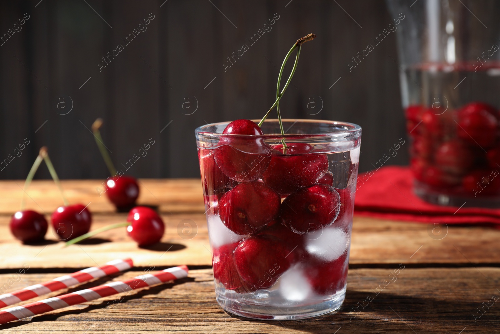 Photo of Sweet red cherries with ice cubes in glass on wooden table