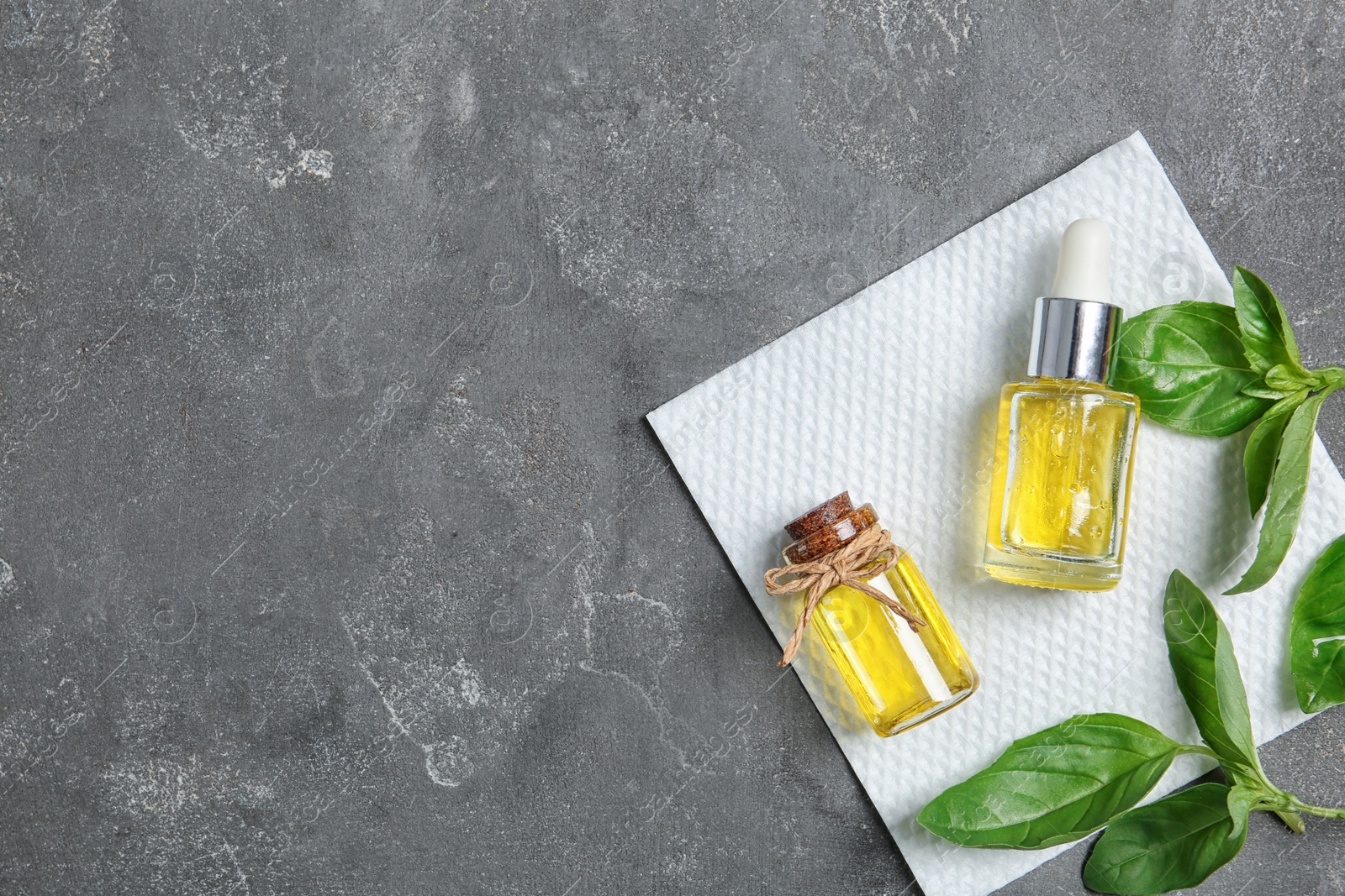 Photo of Bottles of essential basil oil, fresh leaves and space for text on grey background, top view