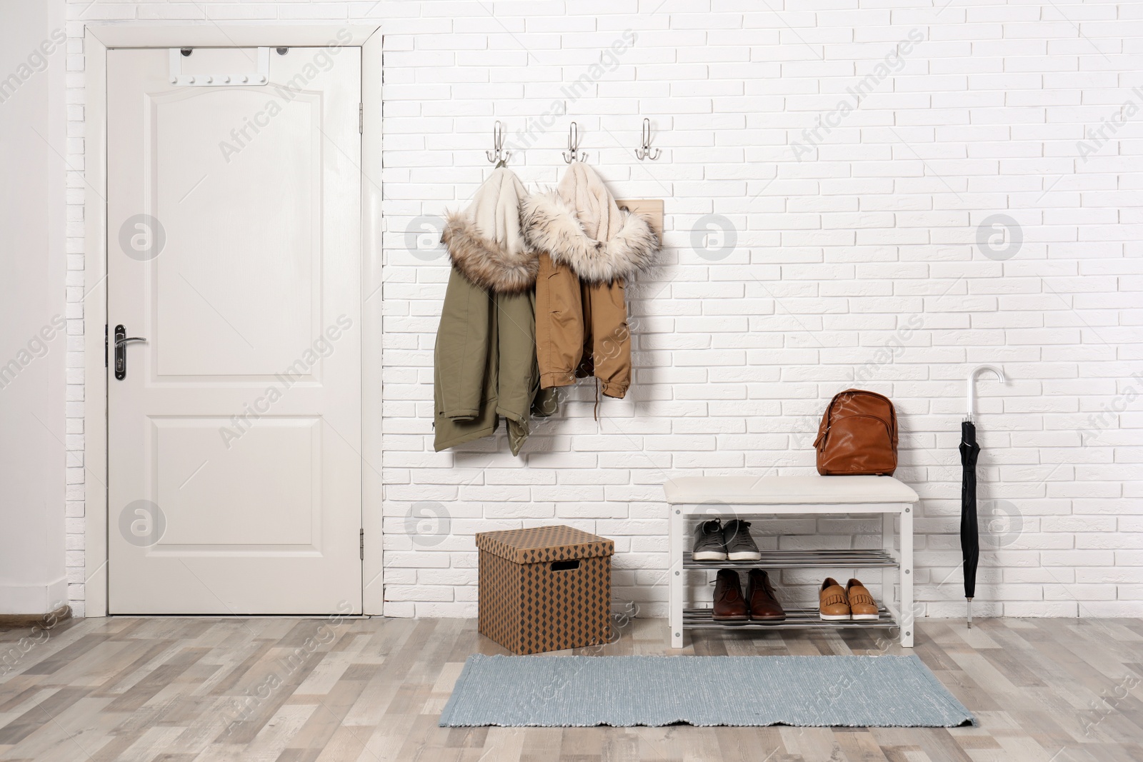 Photo of Stylish hallway interior with shoe rack and hanging clothes on brick wall