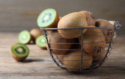 Metal basket with cut and whole fresh kiwis on wooden table, space for text