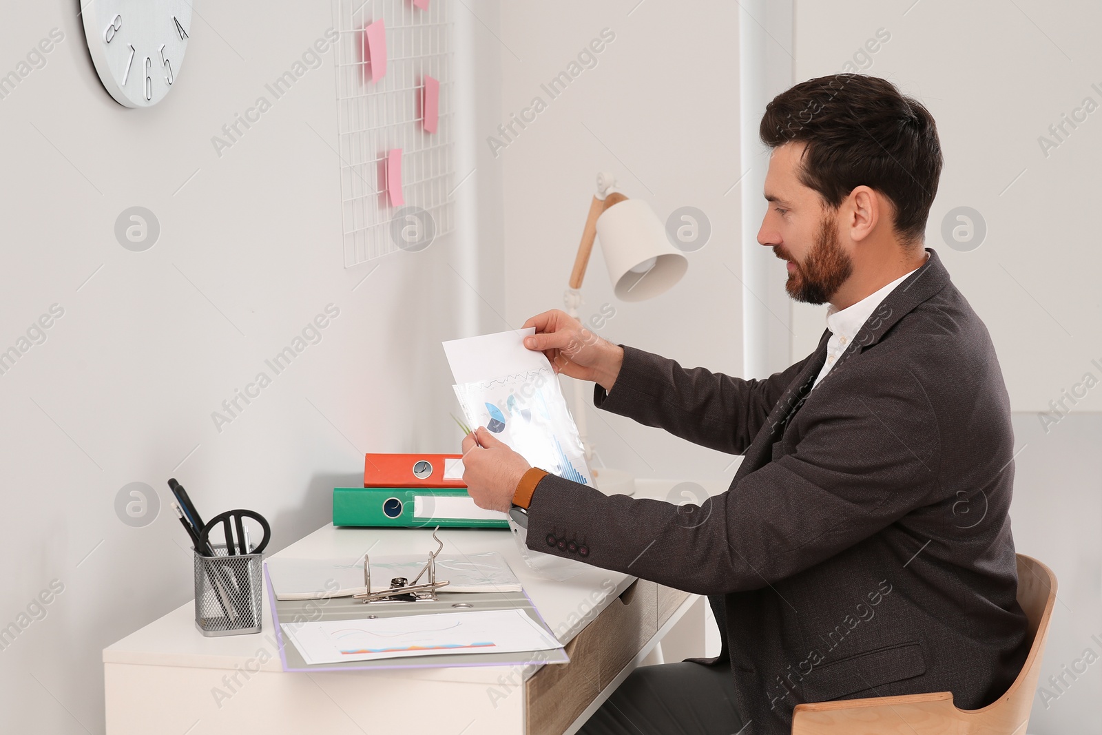 Photo of Businessman putting document into punched pocket at white table in office