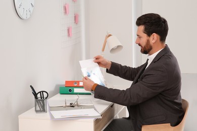 Photo of Businessman putting document into punched pocket at white table in office