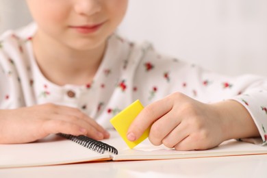 Photo of Girl using eraser at white desk, closeup