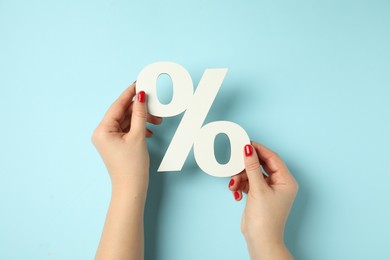 Photo of Woman holding percent sign on light blue background, closeup