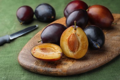 Many tasty ripe plums and wooden board on green fabric, closeup