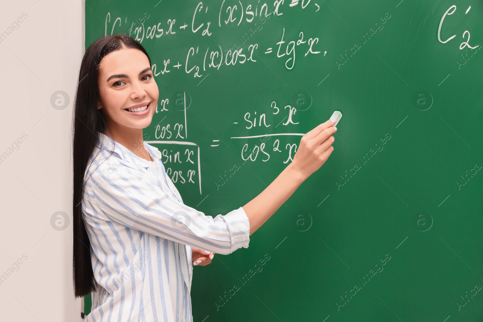 Photo of Happy teacher explaining mathematics at chalkboard in classroom