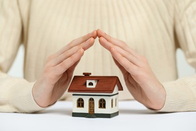 Photo of Home security concept. Woman covering house model at white table, closeup