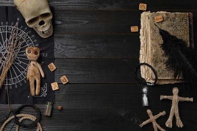 Photo of Voodoo doll with pins surrounded by ceremonial items on black wooden table, flat lay. Space for text
