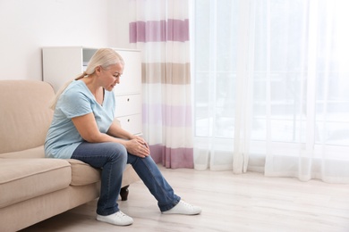 Photo of Senior woman suffering from knee pain at home. Space for text