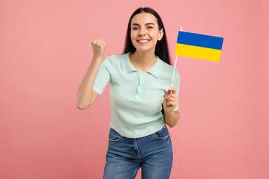 Happy young woman with flag of Ukraine on pink background