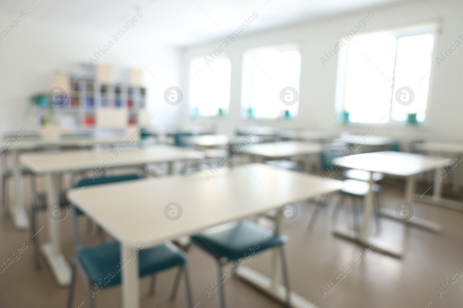 Photo of Blurred view of empty school classroom with desks, windows and chairs