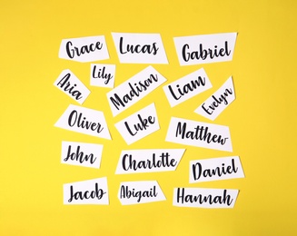 Paper sheets with written different baby names on yellow background, flat lay