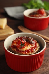 Photo of Baked eggplant with tomatoes and cheese in ramekin on wooden table, closeup