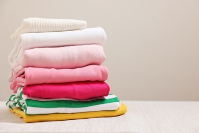 Photo of Stack of folded clothes on wooden table against grey background, space for text