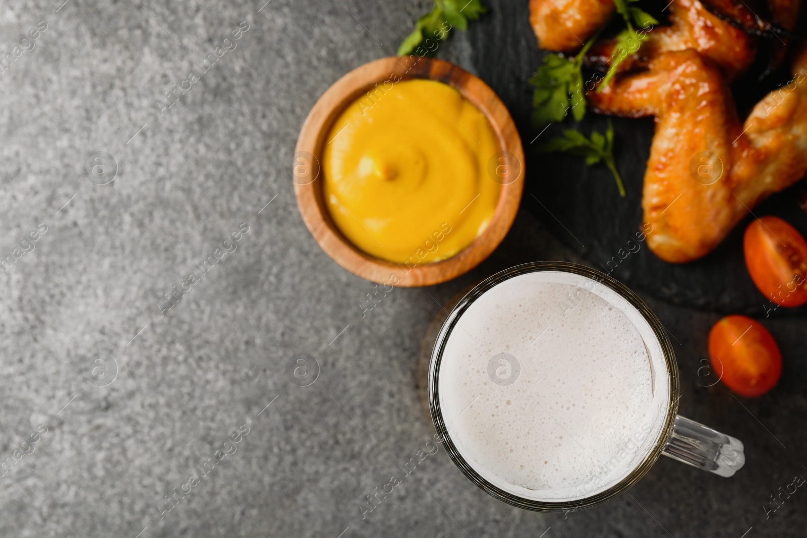Photo of Mug with beer, delicious baked chicken wings and sauce on grey table, flat lay. Space for text