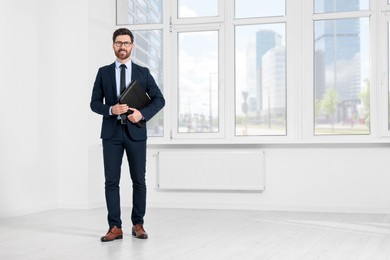 Handsome real estate agent with documents in empty room, space for text