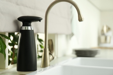 Photo of Modern automatic soap dispenser near sink in kitchen