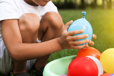 Little boy with basin of water bombs on green grass, closeup