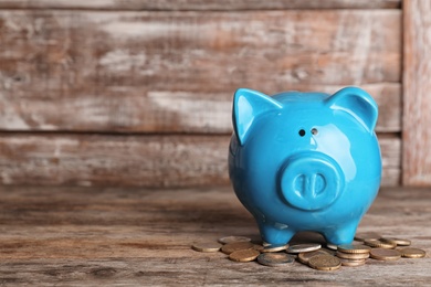 Piggy bank with coins on wooden table. Space for text