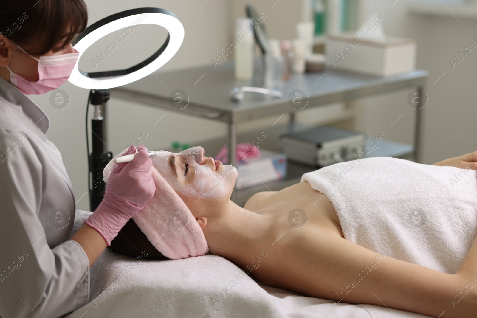 Photo of Cosmetologist applying mask on woman's face in clinic, closeup