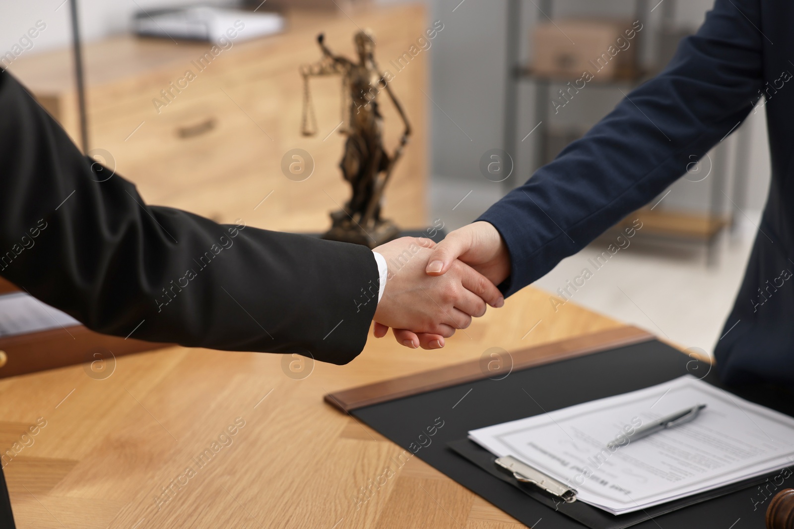 Photo of Notary shaking hands with client at wooden table in office, closeup