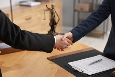 Photo of Notary shaking hands with client at wooden table in office, closeup