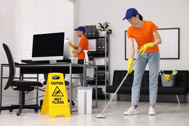 Cleaning service workers cleaning. Bucket with supplies and wet floor sign in office