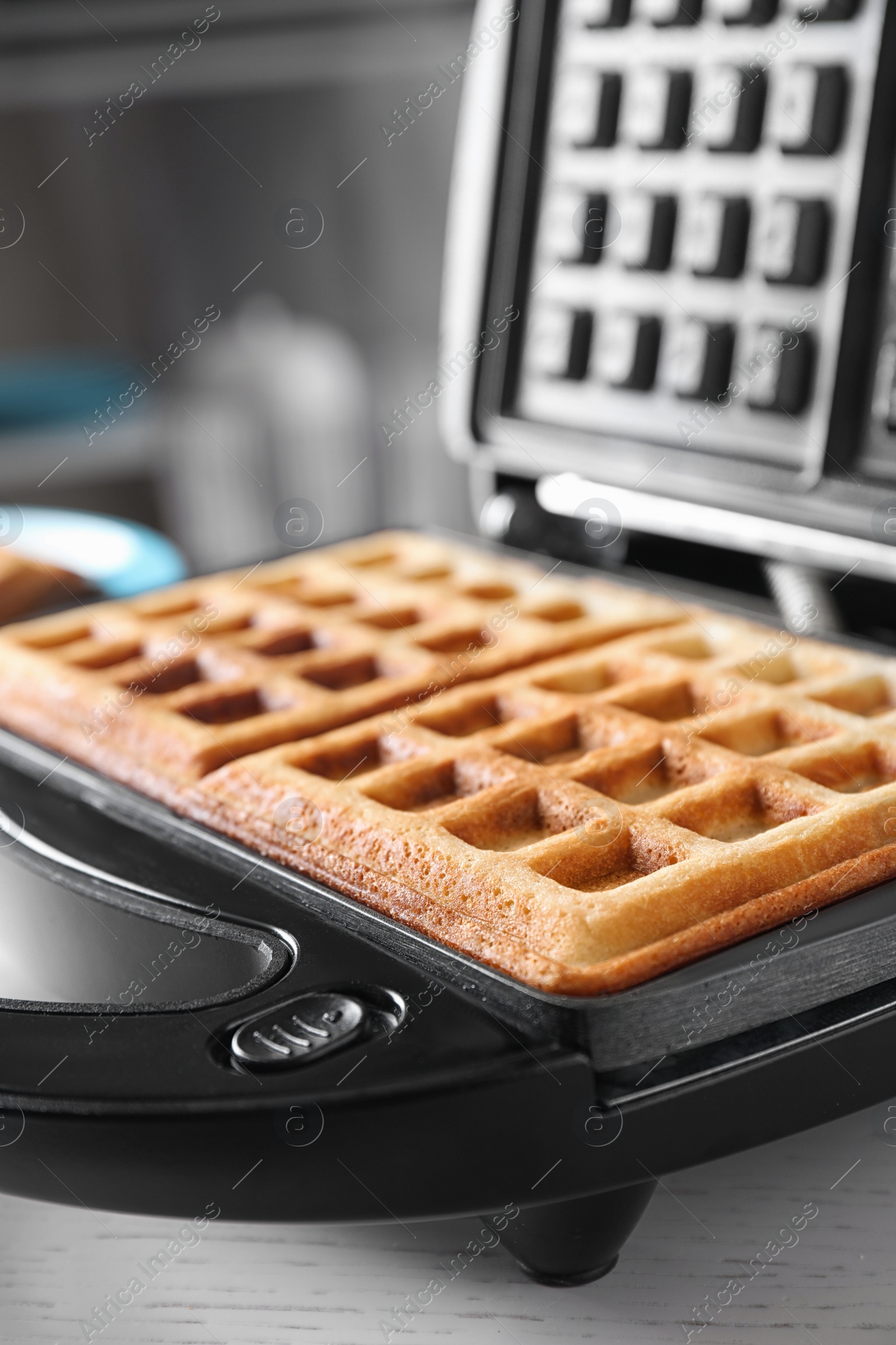 Photo of Modern iron with tasty Belgian waffles on table, closeup