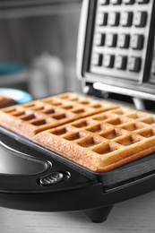 Photo of Modern iron with tasty Belgian waffles on table, closeup