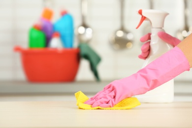 Photo of Woman cleaning table with rag in kitchen, closeup. Space for text