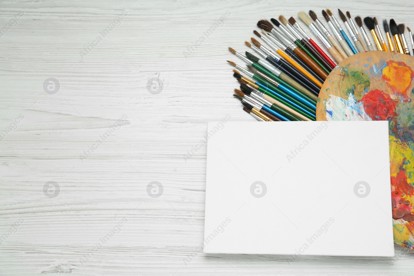 Photo of Blank canvas, brushes and palette on white wooden table, flat lay. Space for text