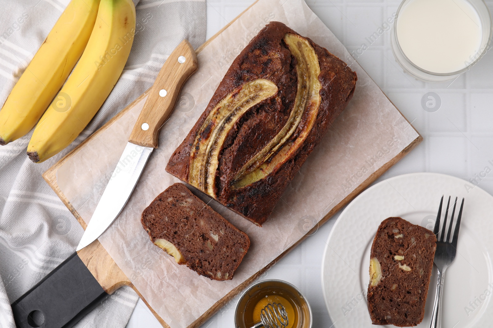 Photo of Delicious banana bread served on white tiled table, flat lay