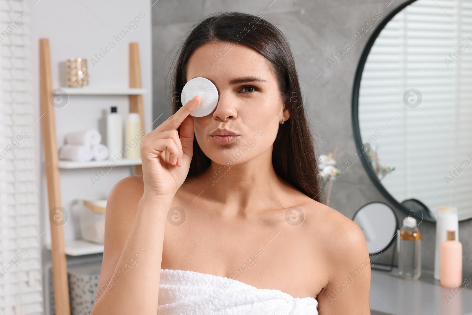 Photo of Young woman cleaning her face with cotton pad in bathroom