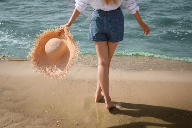 Photo of Young woman with straw hat near sea on sunny day in summer, closeup back view