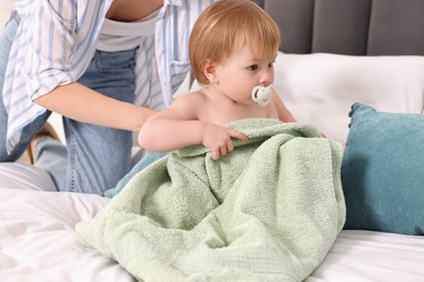 Mother wrapping her cute little baby with towel after bathing on bed