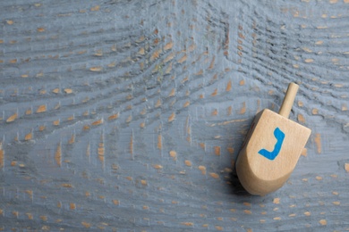 Photo of Hanukkah traditional dreidel with letter Nun on grey wooden table, top view. Space for text