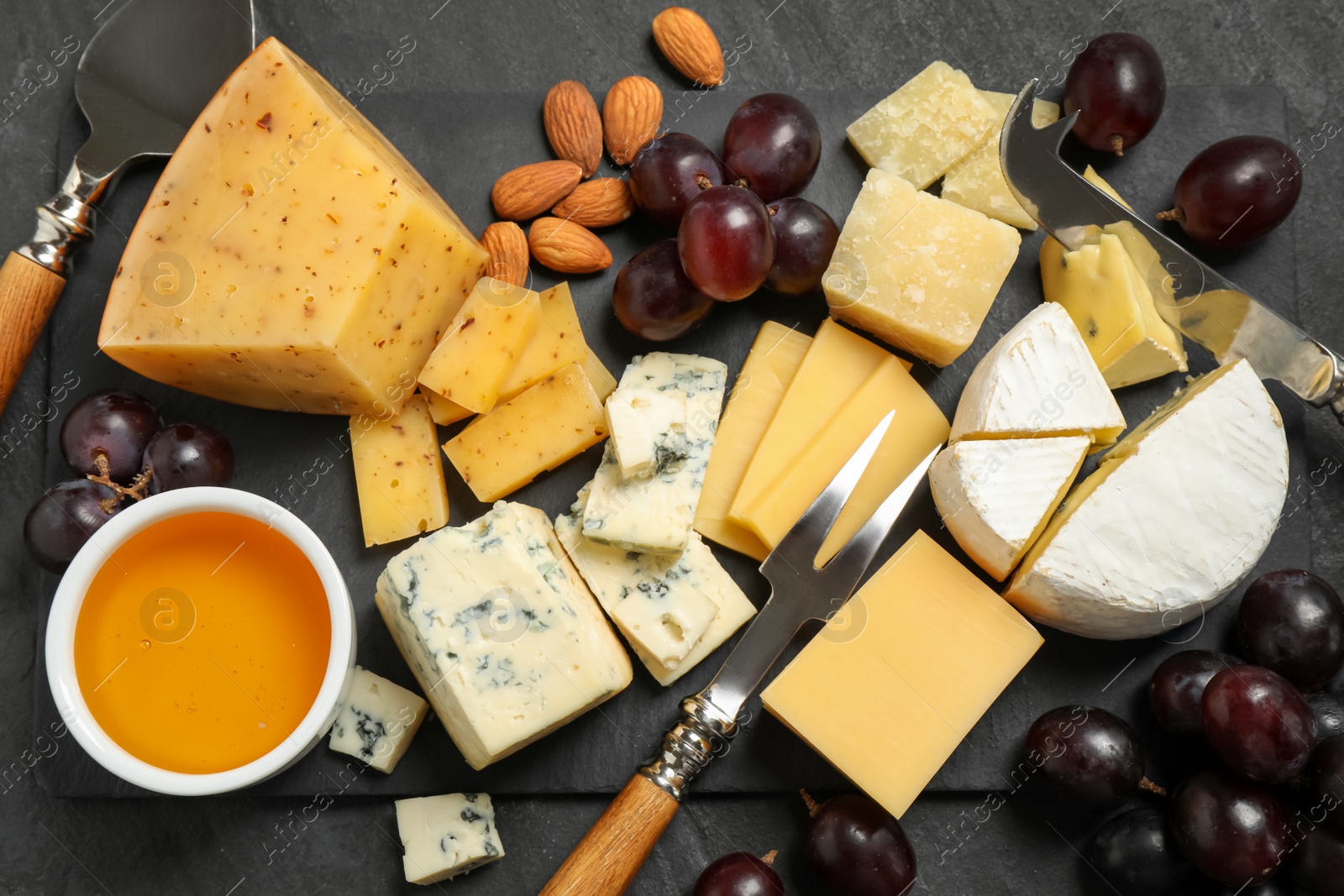 Photo of Cheese platter with specialized knives and fork on black table, flat lay