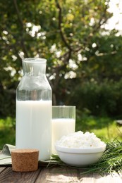 Photo of Tasty fresh milk and cottage cheese on wooden table outdoors