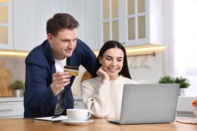 Photo of Happy couple with laptop and credit card shopping online in kitchen