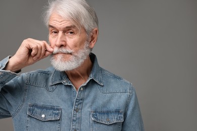 Senior man touching mustache on grey background, space for text