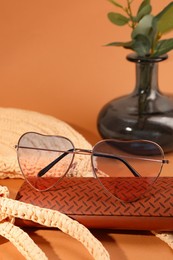 Photo of Stylish heart shaped sunglasses and brown leather case on pale orange background