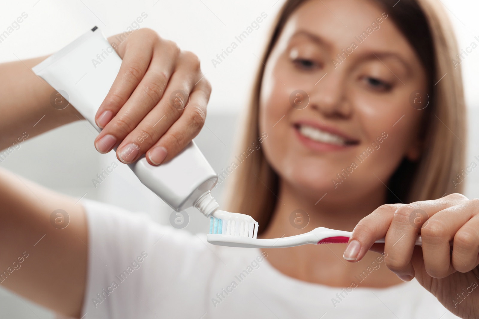 Photo of Young woman applying toothpaste onto brush in bathroom, focus on hands