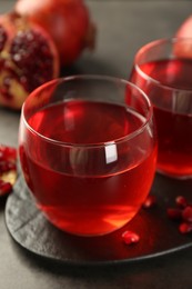 Photo of Tasty pomegranate juice in glasses on grey table, closeup