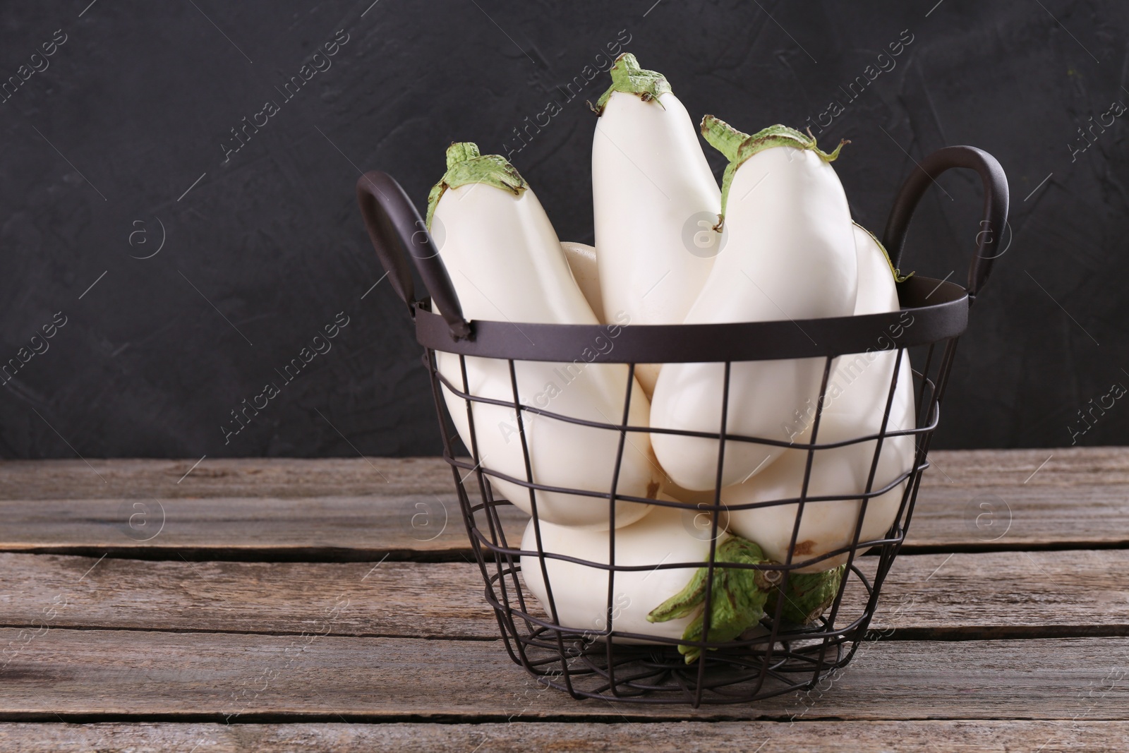 Photo of Fresh white eggplants in metal basket on wooden table, space for text