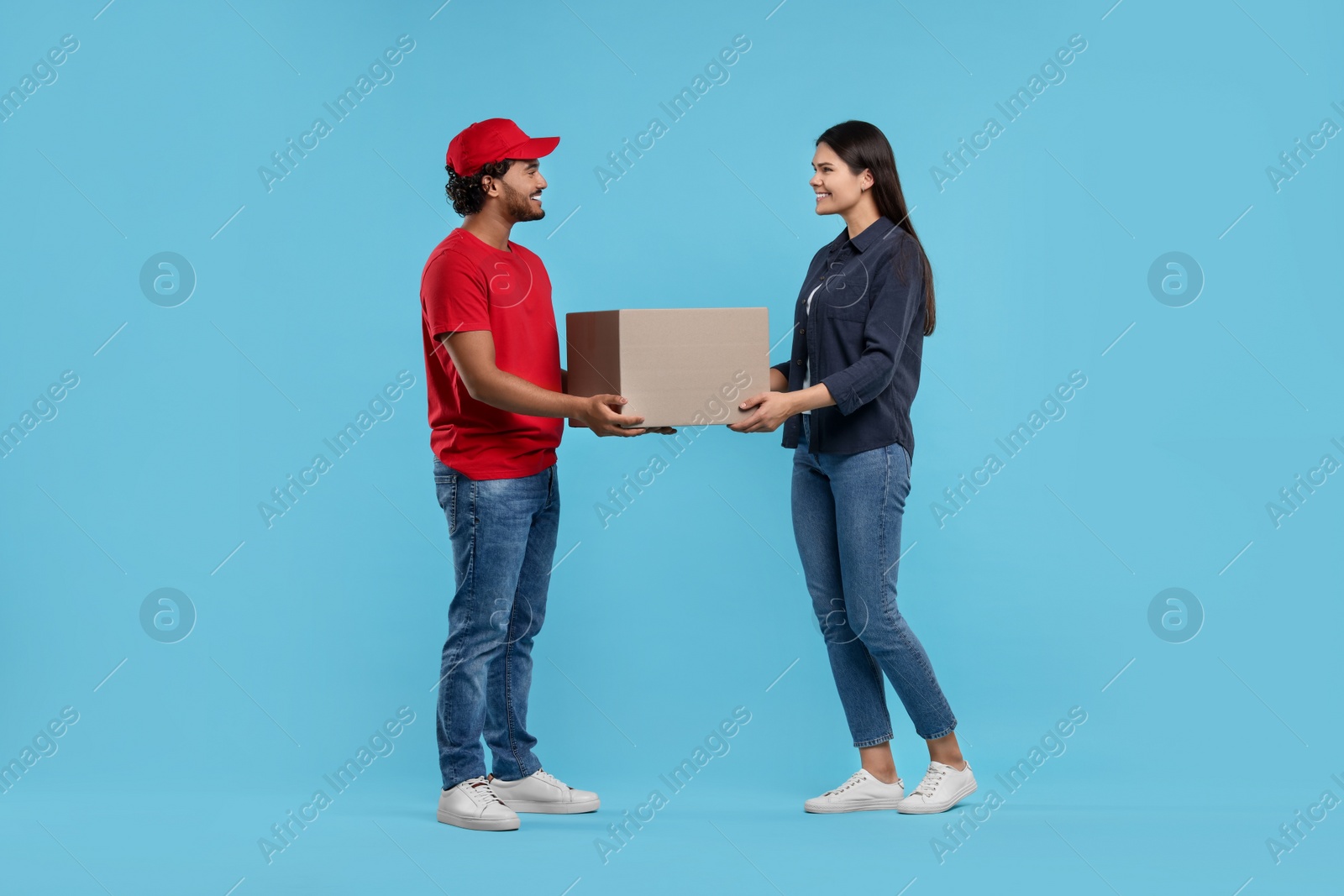 Photo of Smiling courier giving parcel to receiver on light blue background