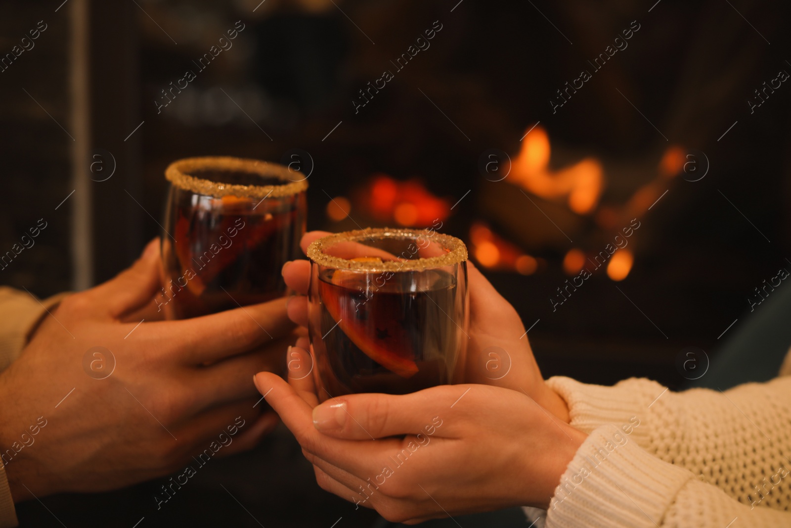 Photo of Couple with tasty mulled wine near fireplace indoors, closeup