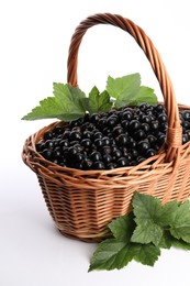 Photo of Ripe blackcurrants and leaves in wicker basket on white background