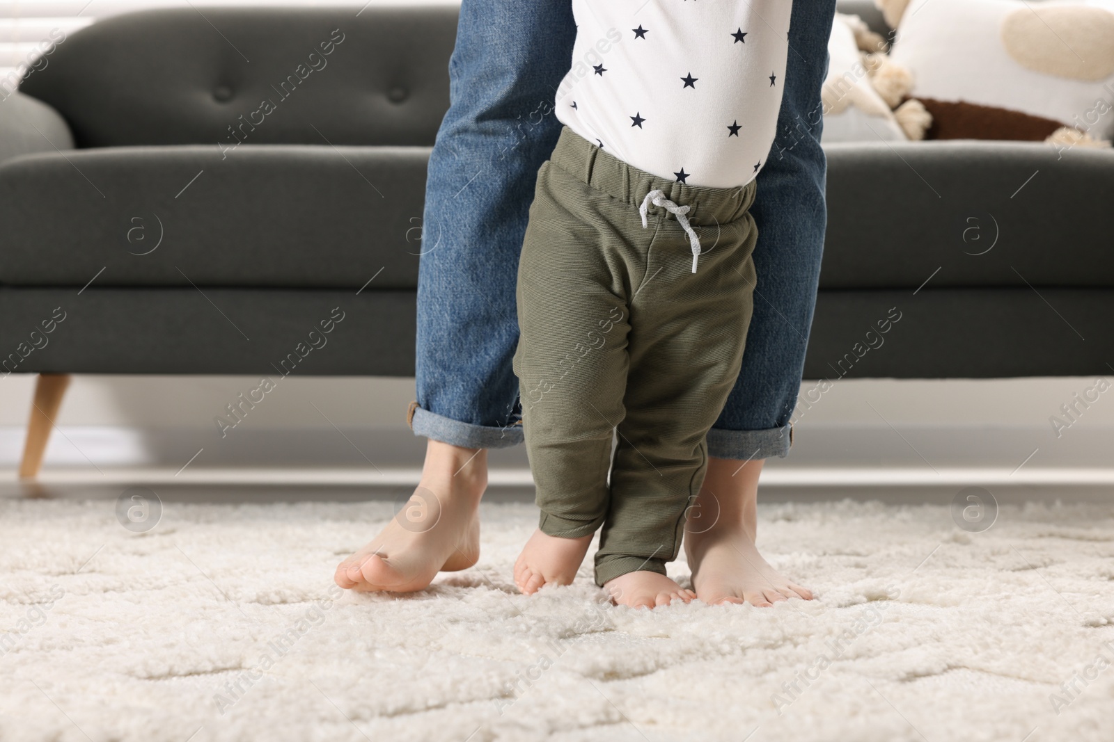 Photo of Mother supporting her baby son while he learning to walk on carpet at home, closeup